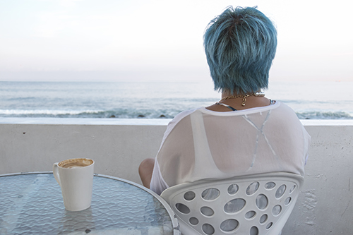 Woman sitting by a low wall with a cup of coffee looking out ove