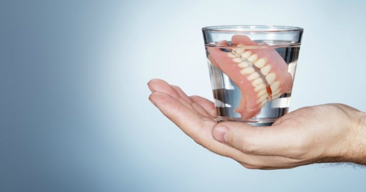hand holding dentures in glass of water