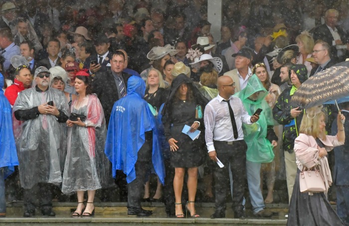 Crowds rushed to take cover under umbrellas and ponchos to watch the races from outside. Source: Getty.