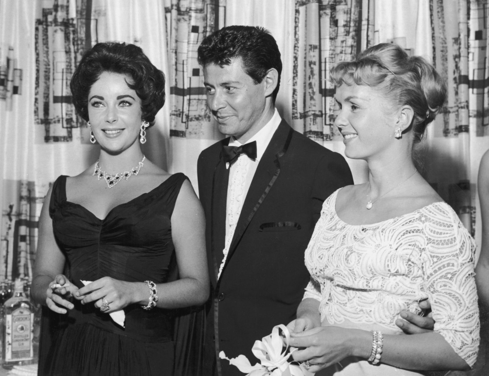 Eddie Fisher stands with arm around wife Debbie Reynolds and smiles while looking at Elizabeth Taylor. Source: Getty.